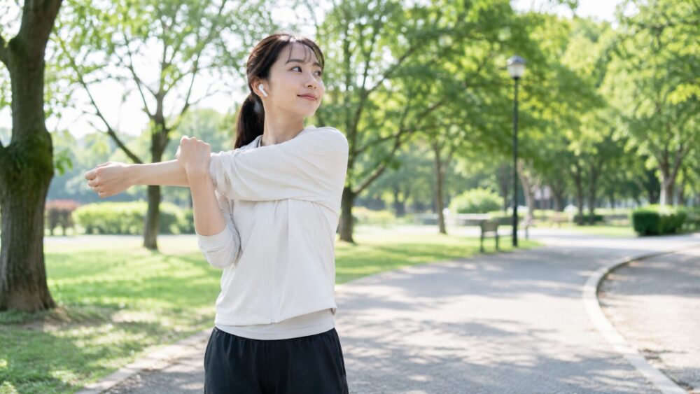 公園で女性がイヤホンで曲を聴きながらストレッチをしている